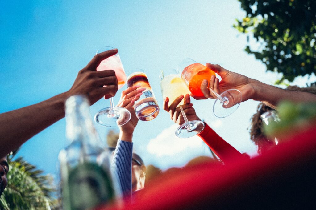 Thomas Henry Daydrinking. Freunde halten Drink-Gläser in die Luft, blauer Himmel.